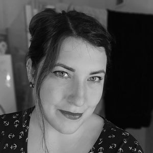 Gründerin Anne. Sie hat dunkle Haare, die im Dutt hochgesteckt sind, blickt lächelnd in die Kamera und trägt dunklen Lippenstift.