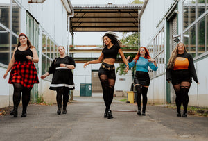 Overknee-Strümpfe und Strumpfhosen an 5 Frauen, die nebeneinander versetzt auf einer Straße zwischen Industriegebäuden laufen.