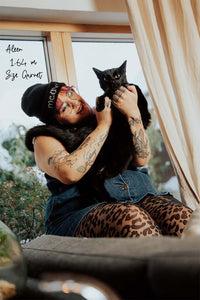 Schwarze Leo-Muster Strumpfhose an Plus Size Model, das einen schwarzen Kater hält und auf einer Fensterbank sitzt.