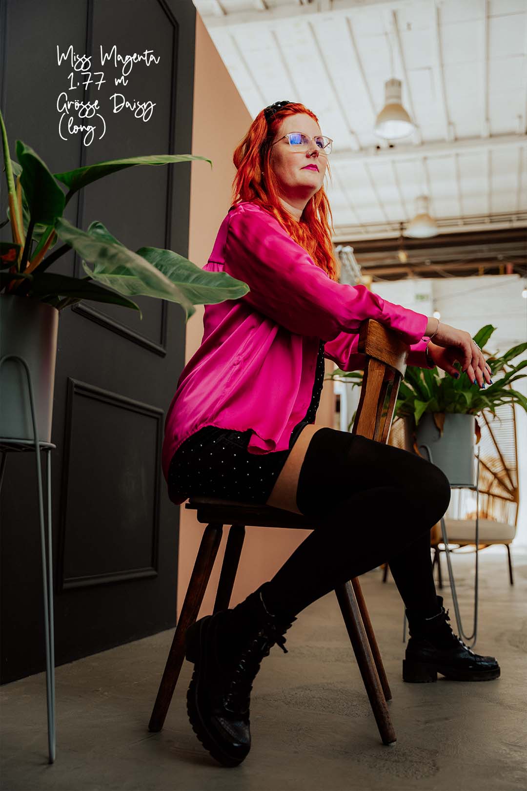 Schwarze Kniestrümpfe an einem 1,77 m großen Model, das auf einem Stuhl sitzt. Sie trägt eine pinke Bluse und hat rote Haare und eine Brille.