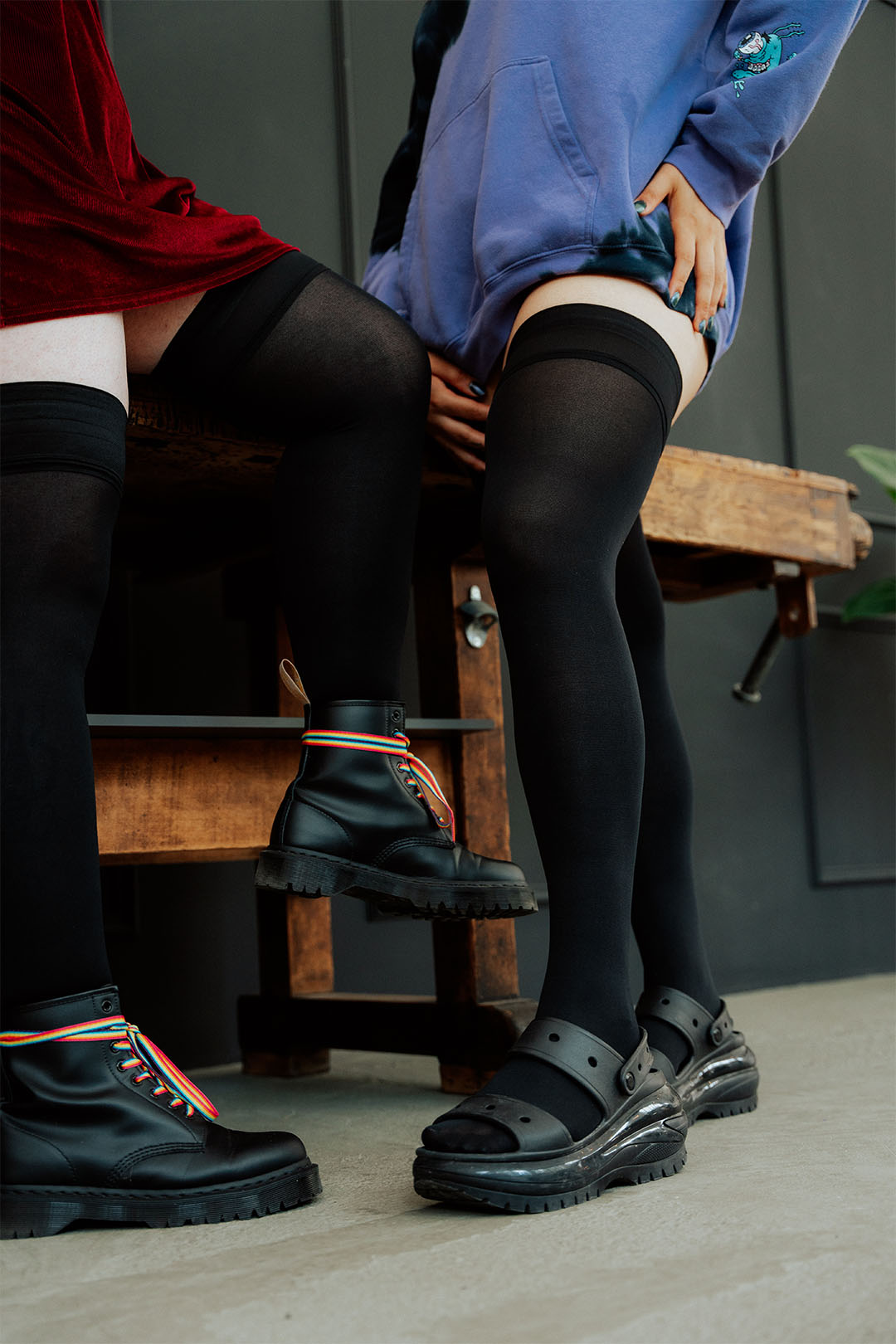 Extra lange Overknee-Strümpfe an den Beinen zweier Frauen, die auf einer Werkbank sitzen.