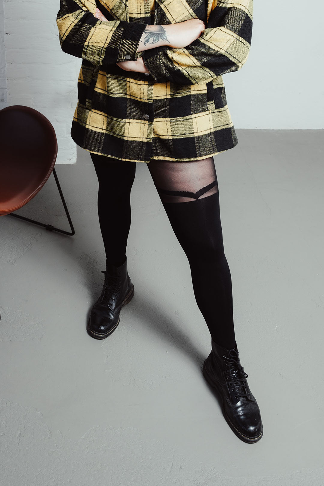 Strumpfhose im Overknee-Look an den Beinen einer jungen Frau, die ein kariertes Hemd trägt und schwarze Schuhe. 