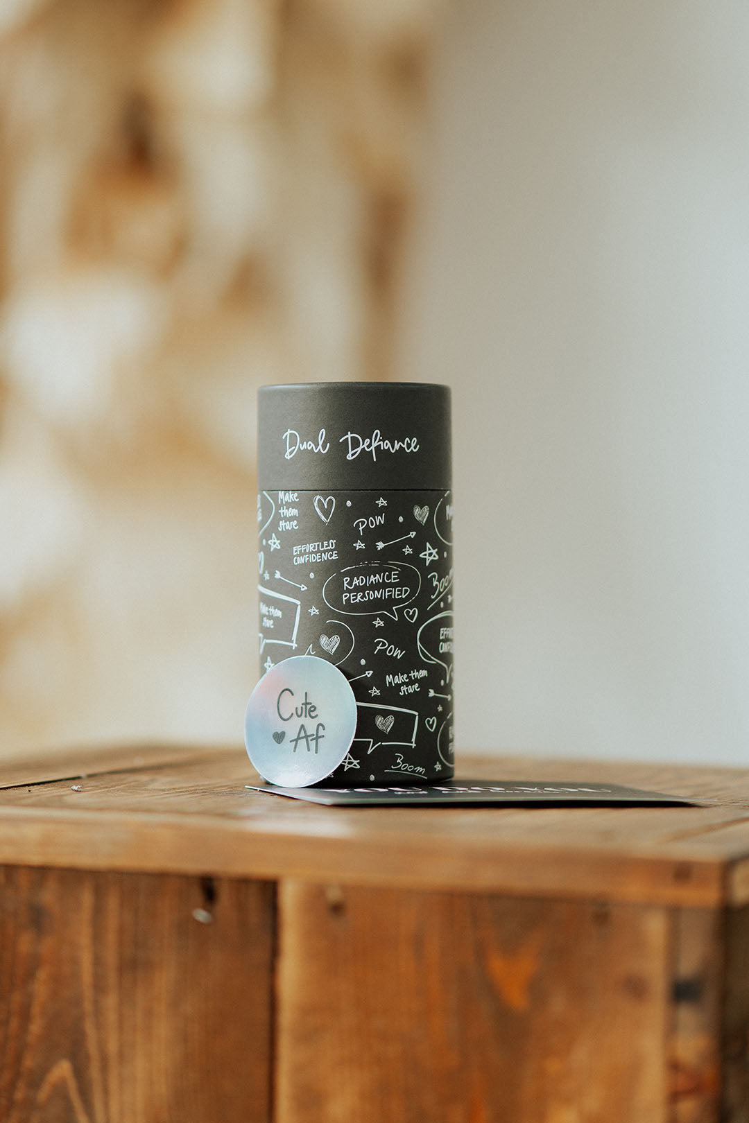 Schwarze Dual Defiance Paper Tube, Verpackung für Strumpfhosen und Strumpfwaren. Daneben eine Postkarte und ein Sticker.