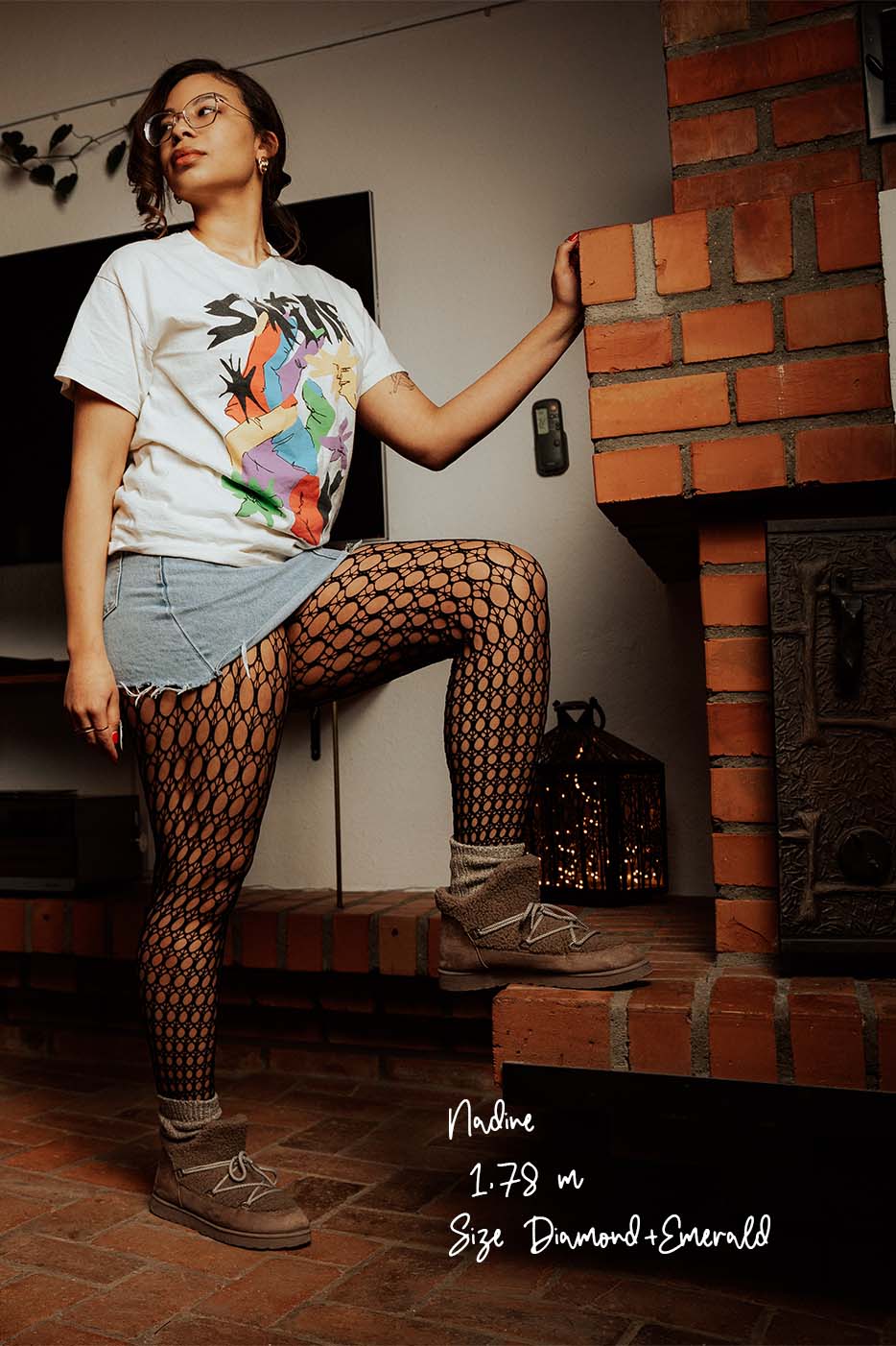 Netzstrumpfhosen mit Kreis-Muster, leger kombiniert mit Jeans-Minirock, bedrucktem T-Shirt und Fell-Boots. Das Model ist 178 cm groß und trägt eine Brille.